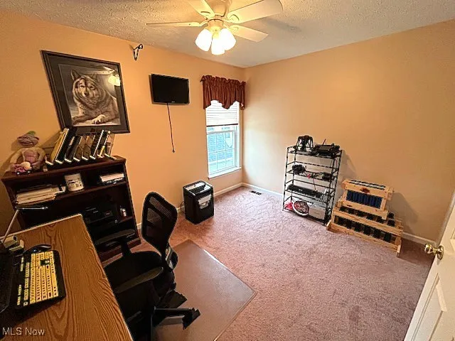 Carpeted office featuring a textured ceiling, a ceiling fan, and baseboards