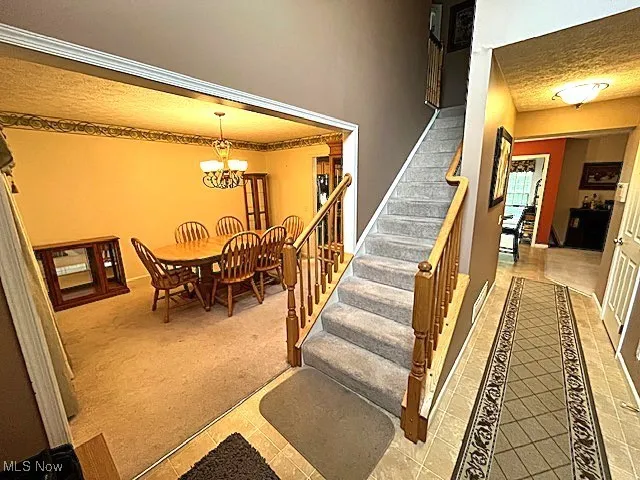 Stairway featuring tile patterned floors, carpet, a chandelier, baseboards, and a towering ceiling