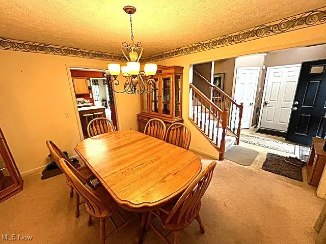 Carpeted dining room with a chandelier, a textured ceiling, stairway, and baseboards