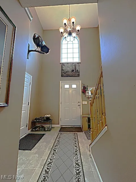Foyer entrance with a chandelier, stairs, baseboards, inlaid floor details, and a towering ceiling