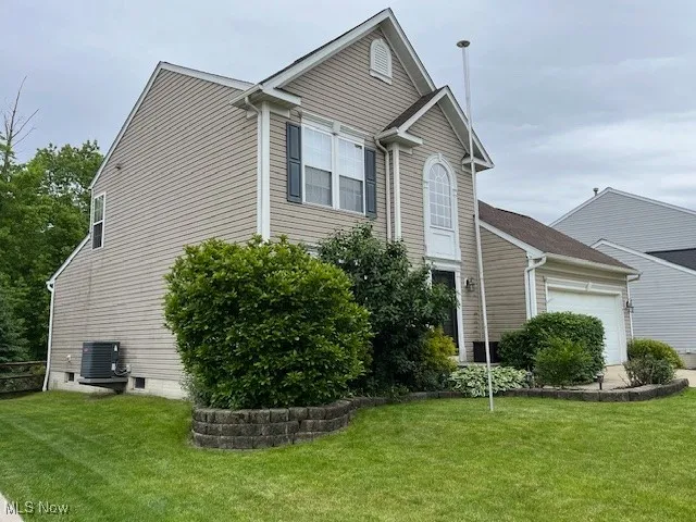 View of side of home with an attached garage, central AC unit, and a yard