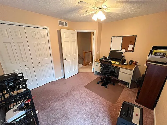 Carpeted home office featuring a ceiling fan and a textured ceiling