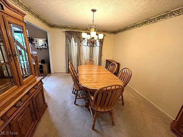 Dining room with a chandelier, a textured ceiling, light carpet, and baseboards