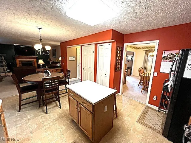 Kitchen featuring freestanding refrigerator, a chandelier, a textured ceiling, a kitchen island, and a brick fireplace