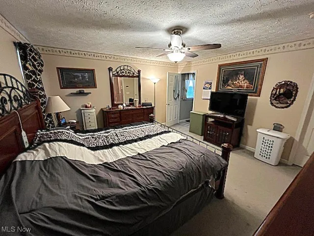Bedroom with light colored carpet, a textured ceiling, a ceiling fan, and ensuite bathroom