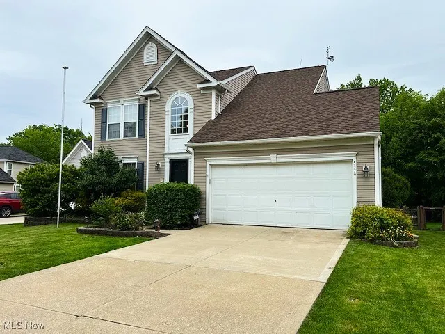 Traditional home with a front yard, concrete driveway, an attached garage, and roof with shingles