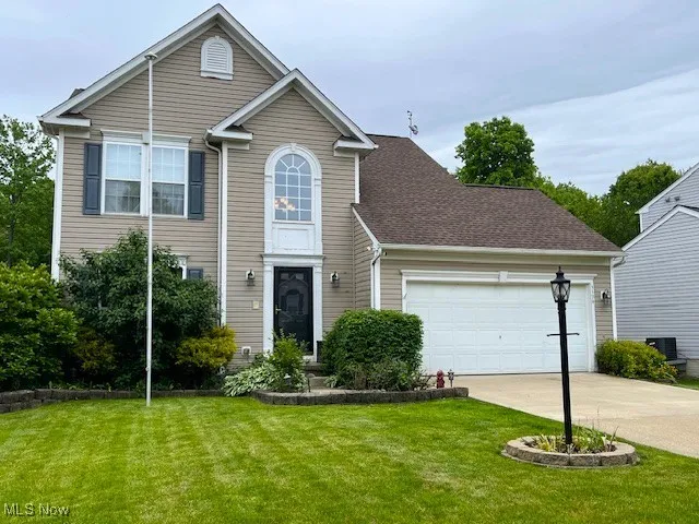 Traditional-style home featuring a garage, concrete driveway, a front yard, and central AC unit