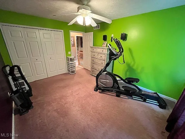 Exercise room featuring a ceiling fan, carpet floors, a textured ceiling, and baseboards