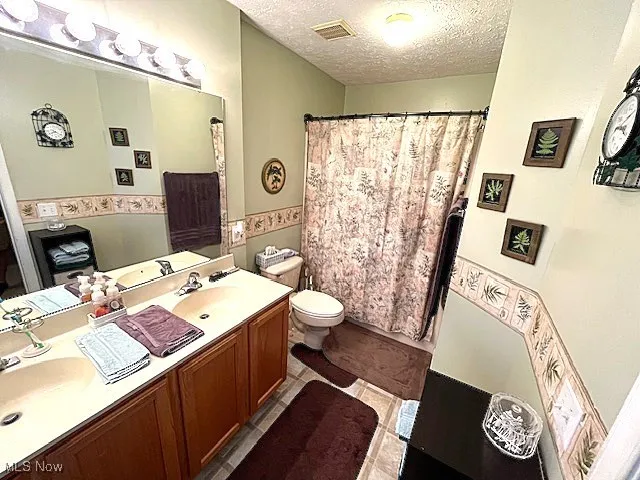 Bathroom with toilet, double vanity, a textured ceiling, curtained shower, and tile patterned floors