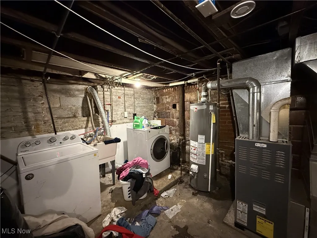 Unfinished below grade area with gas water heater, heating unit, and washer and clothes dryer