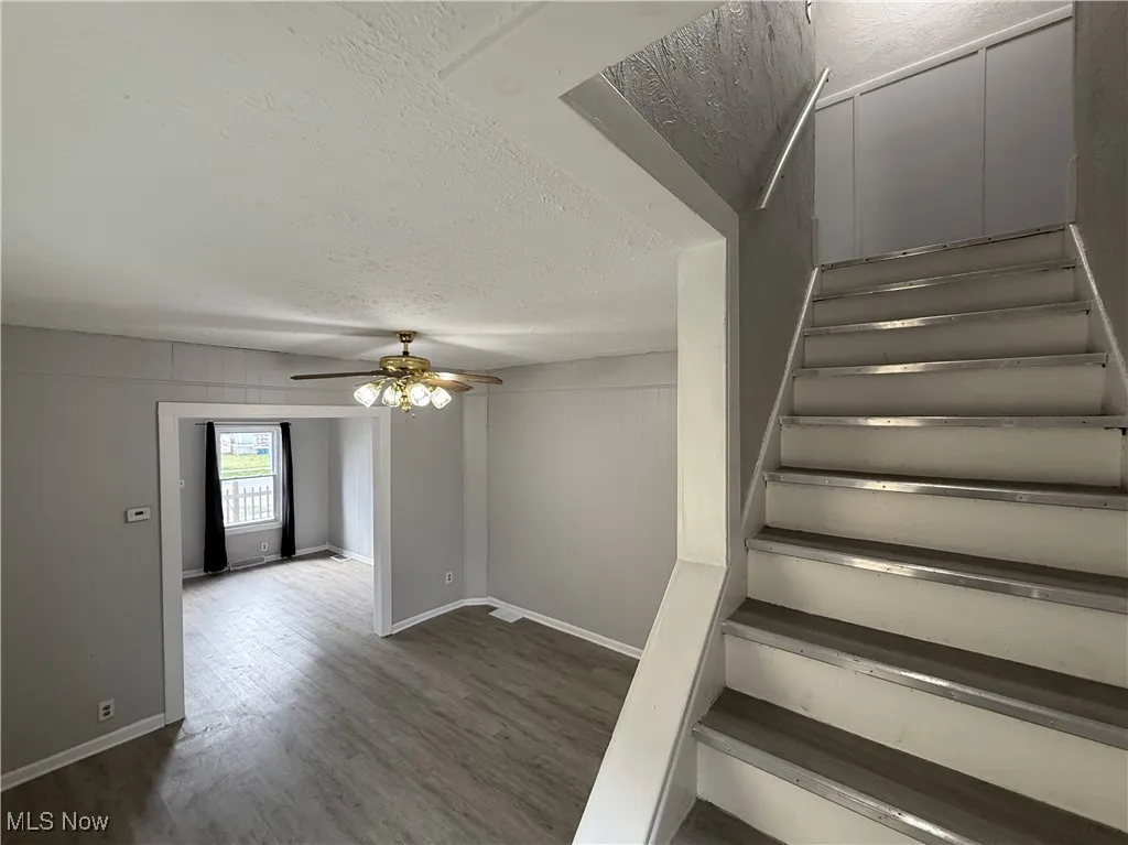 Staircase with a ceiling fan, baseboards, wood finished floors, and a textured ceiling