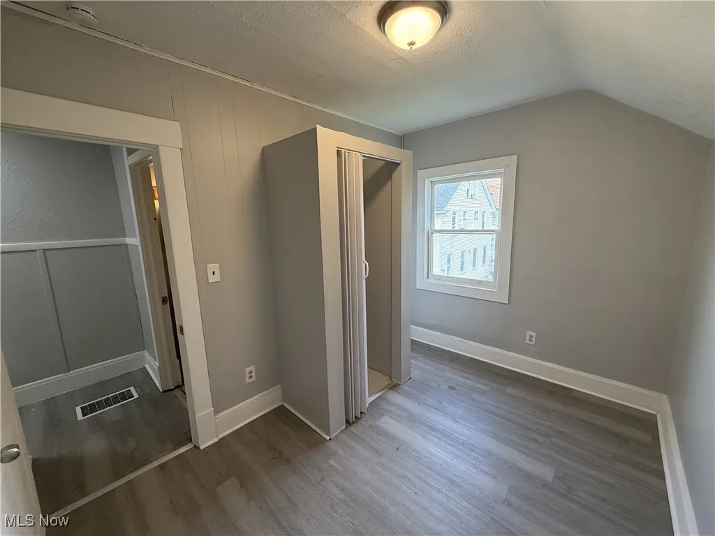Unfurnished bedroom featuring a closet, wood finished floors, visible vents, a textured ceiling, and lofted ceiling