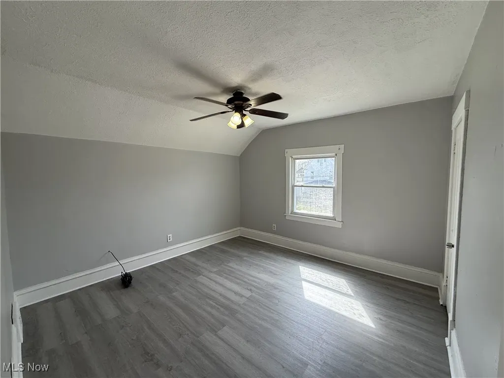 Bonus room with baseboards, dark wood-style floors, a ceiling fan, a textured ceiling, and lofted ceiling