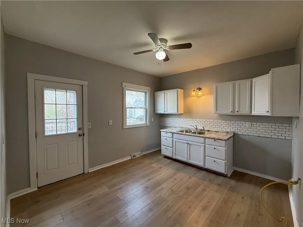 Kitchen with white cabinetry, decorative backsplash, a sink, light wood-style floors, and a ceiling fan