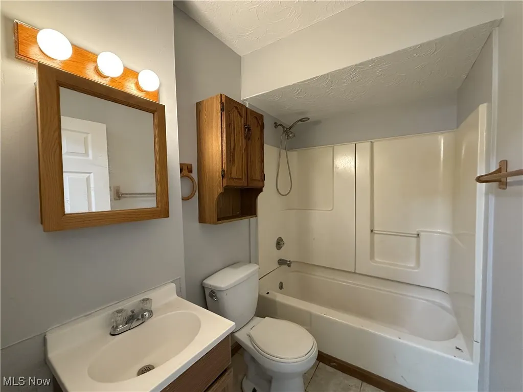 Full bathroom featuring tile patterned floors, bathing tub / shower combination, toilet, vanity, and a textured ceiling