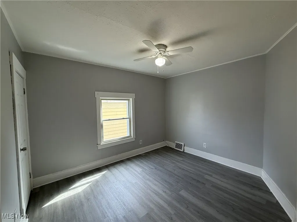 Unfurnished room with visible vents, ceiling fan, dark wood-style floors, baseboards, and ornamental molding