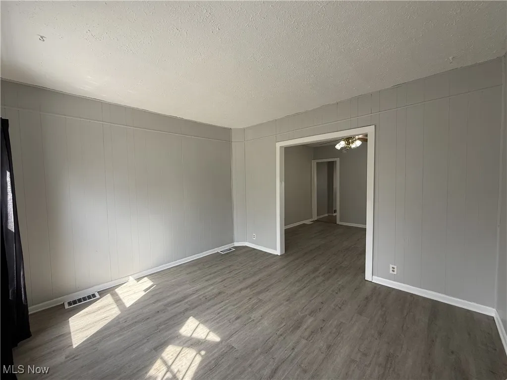 Empty room with a textured ceiling, wood-style flooring, baseboards, and visible vents