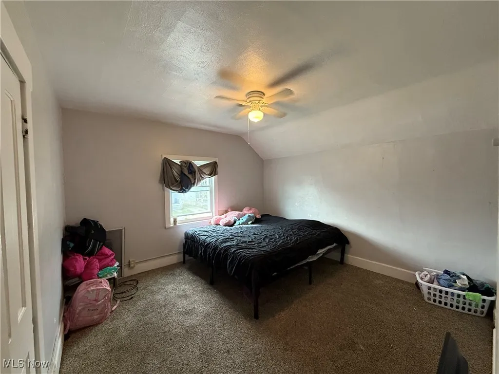 Bedroom with lofted ceiling, a textured ceiling, ceiling fan, baseboards, and carpet