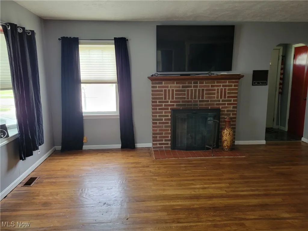 Unfurnished living room with wood finished floors, a fireplace, baseboards, and arched walkways