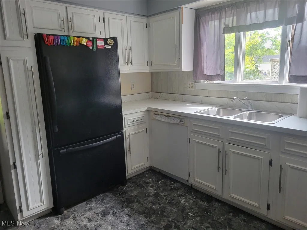 Kitchen featuring freestanding refrigerator, dishwasher, a sink, white cabinetry, and light countertops
