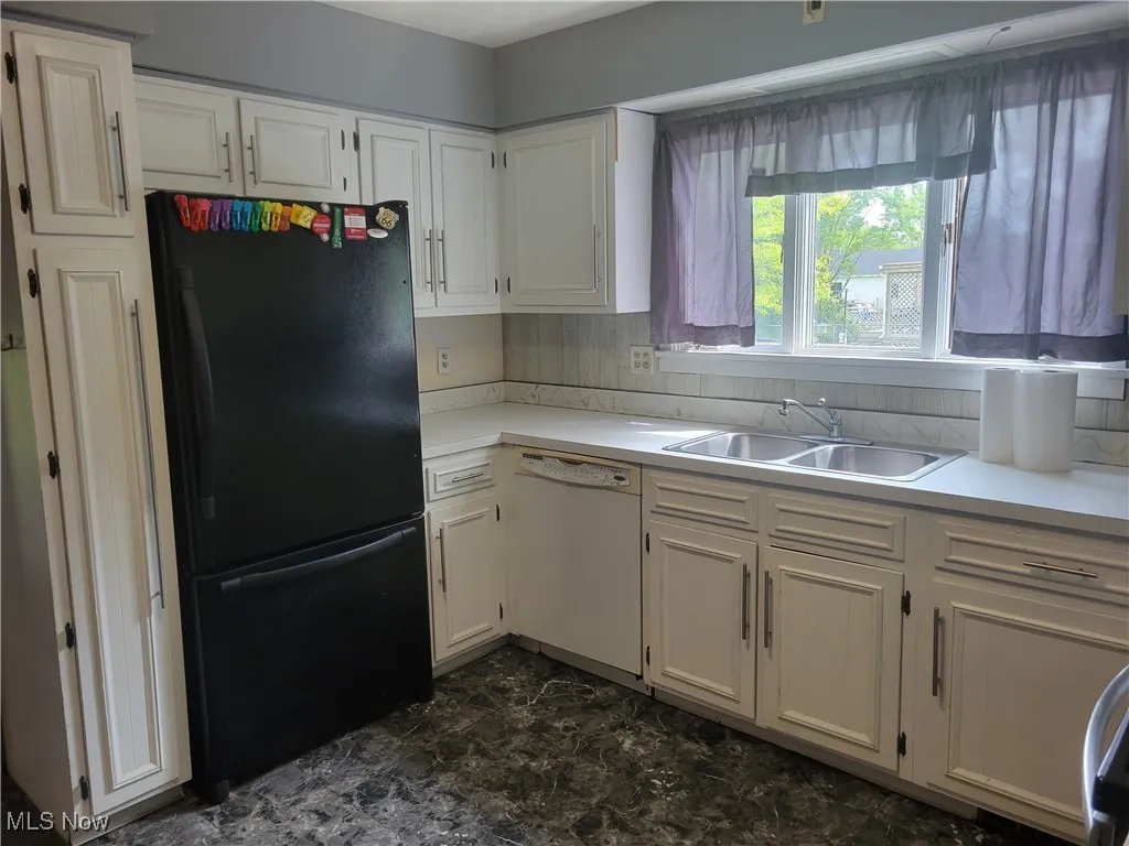 Kitchen with white dishwasher, freestanding refrigerator, a sink, and light countertops