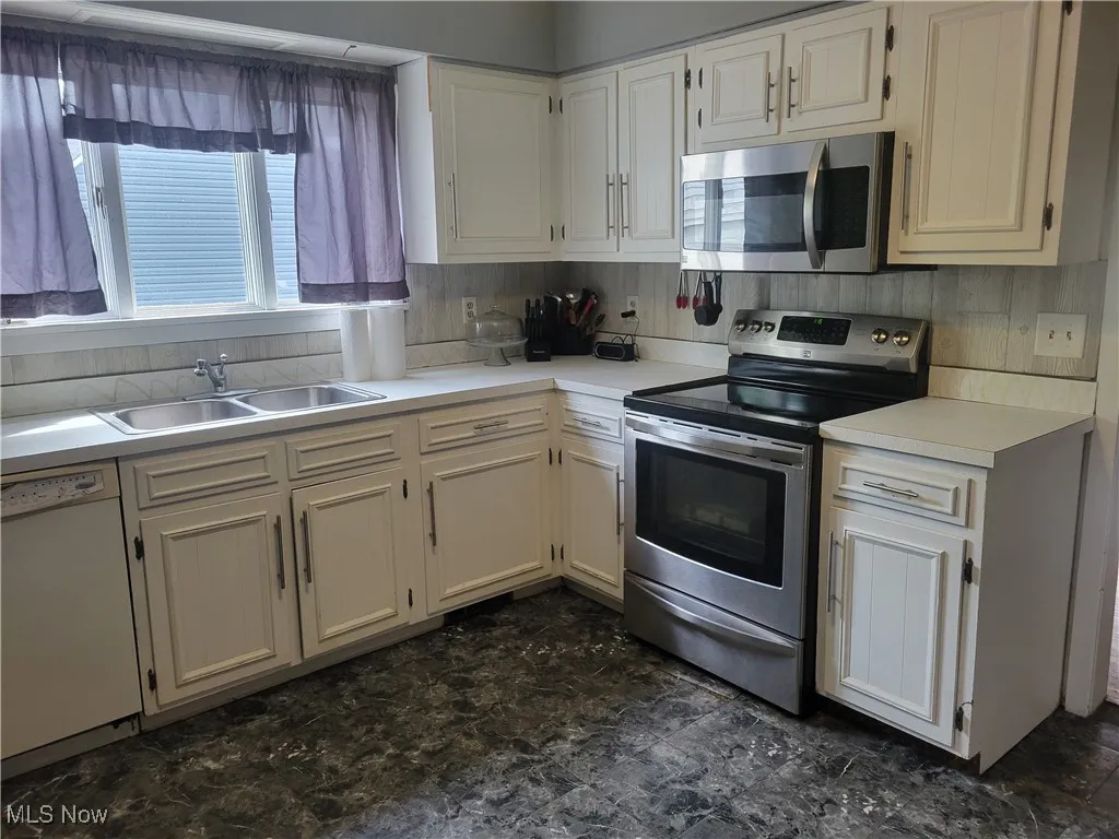 Kitchen with stainless steel appliances, a sink, light countertops, and white cabinetry