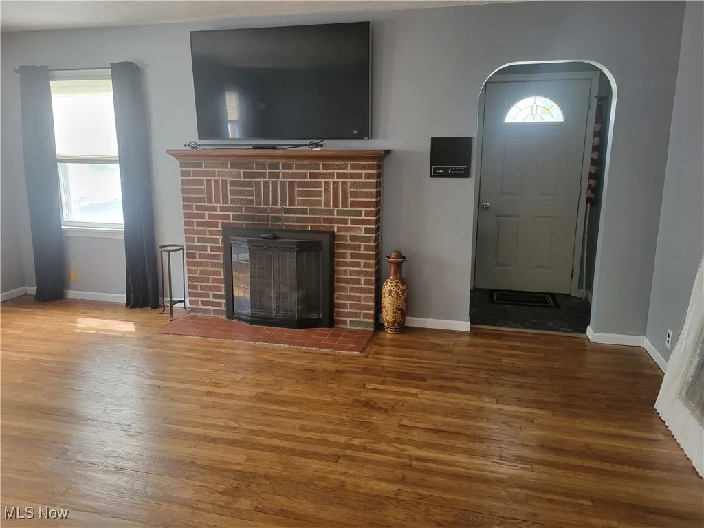 Unfurnished living room featuring wood finished floors, a brick fireplace, and baseboards