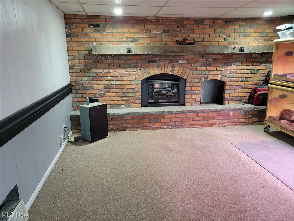 Unfurnished living room featuring carpet floors, a paneled ceiling, a decorative wall, a fireplace, and a wainscoted wall