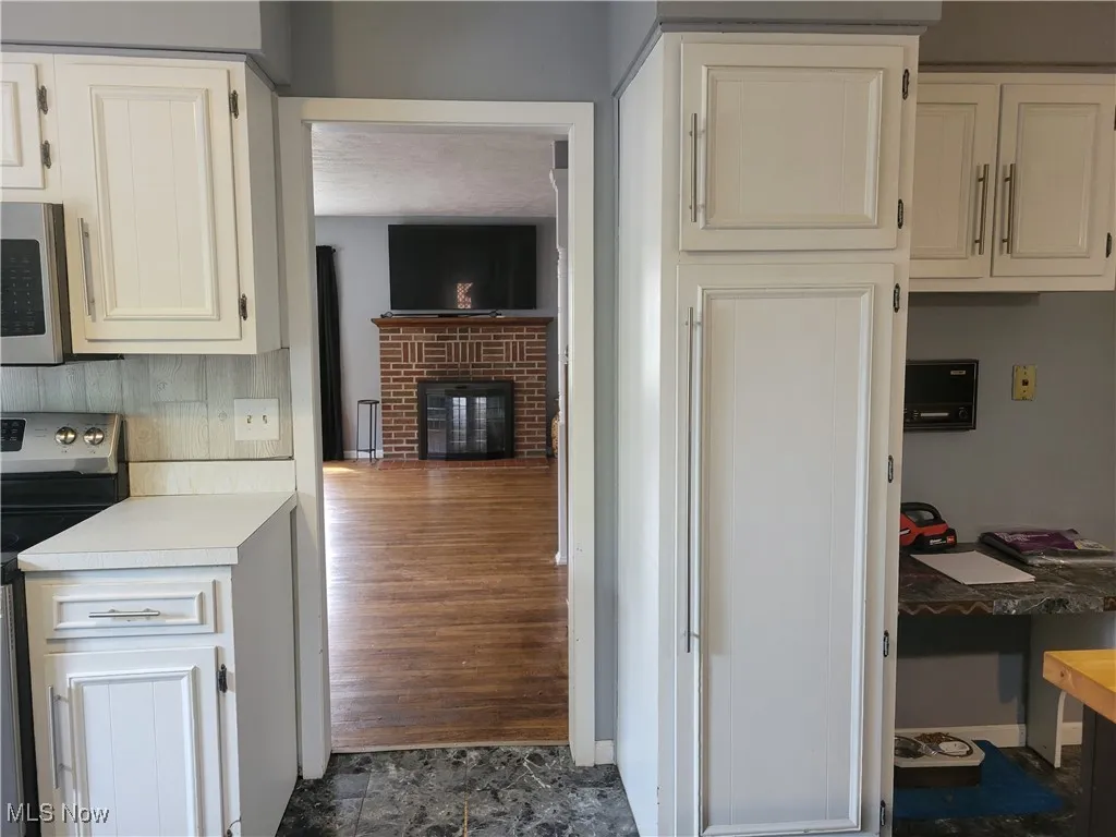 Kitchen featuring appliances with stainless steel finishes, light countertops, a brick fireplace, an office area, and white cabinetry