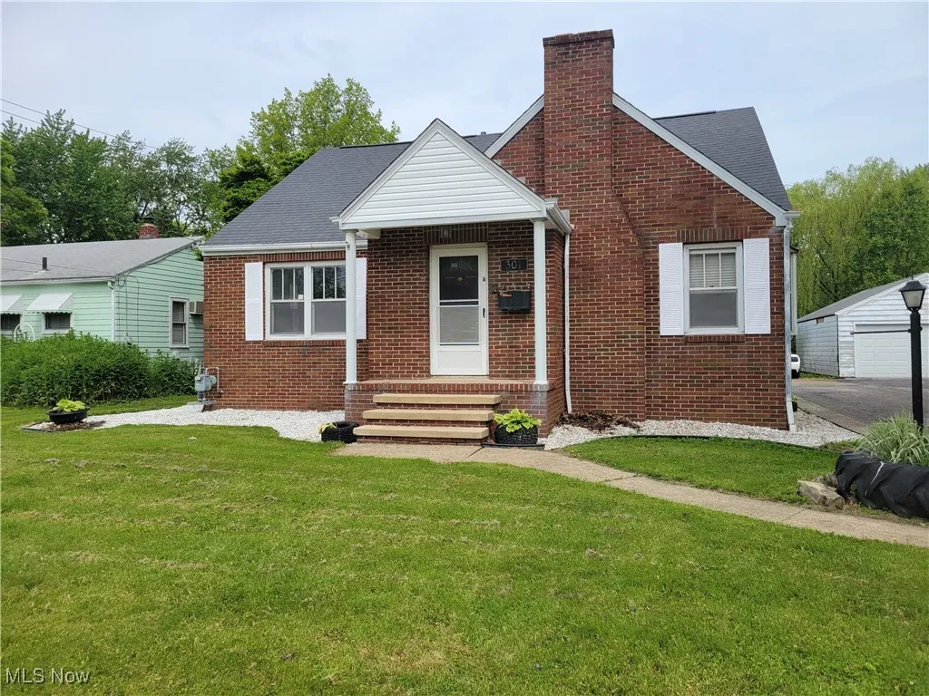 Bungalow-style home with a front yard, brick siding, a chimney, entry steps, and an outdoor structure