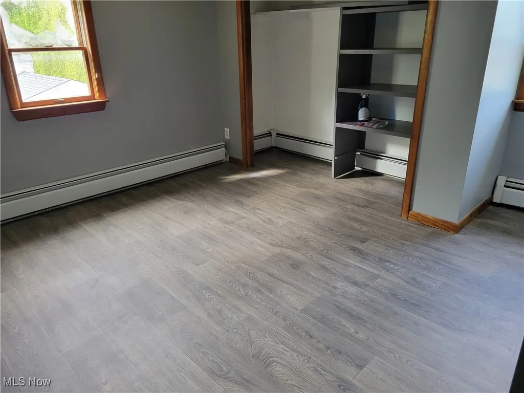 Unfurnished bedroom featuring wood finished floors, baseboard heating, and baseboards