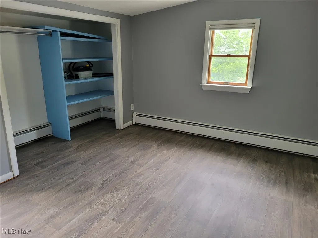 Unfurnished bedroom featuring baseboard heating, wood finished floors, and a closet