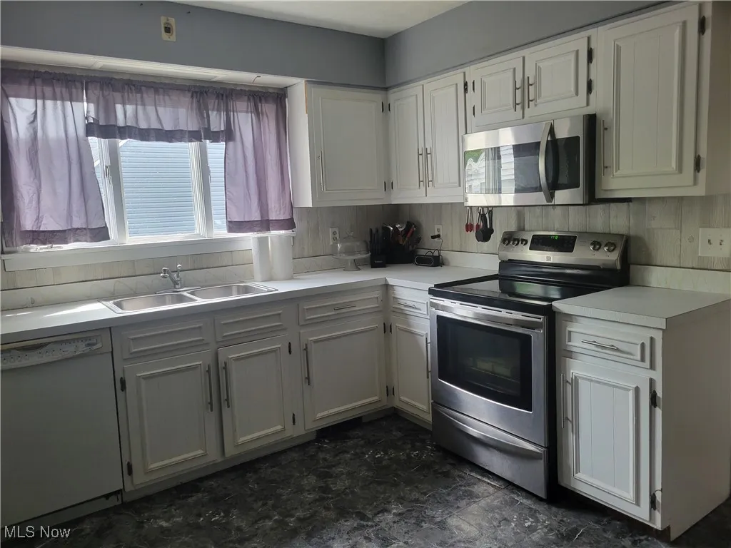 Kitchen with stainless steel appliances, a sink, light countertops, and white cabinetry