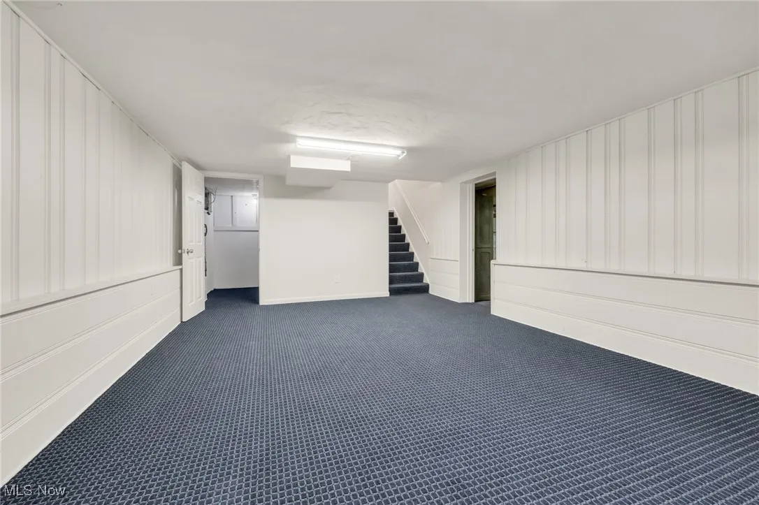 Finished below grade area with dark carpet, stairway, and baseboards