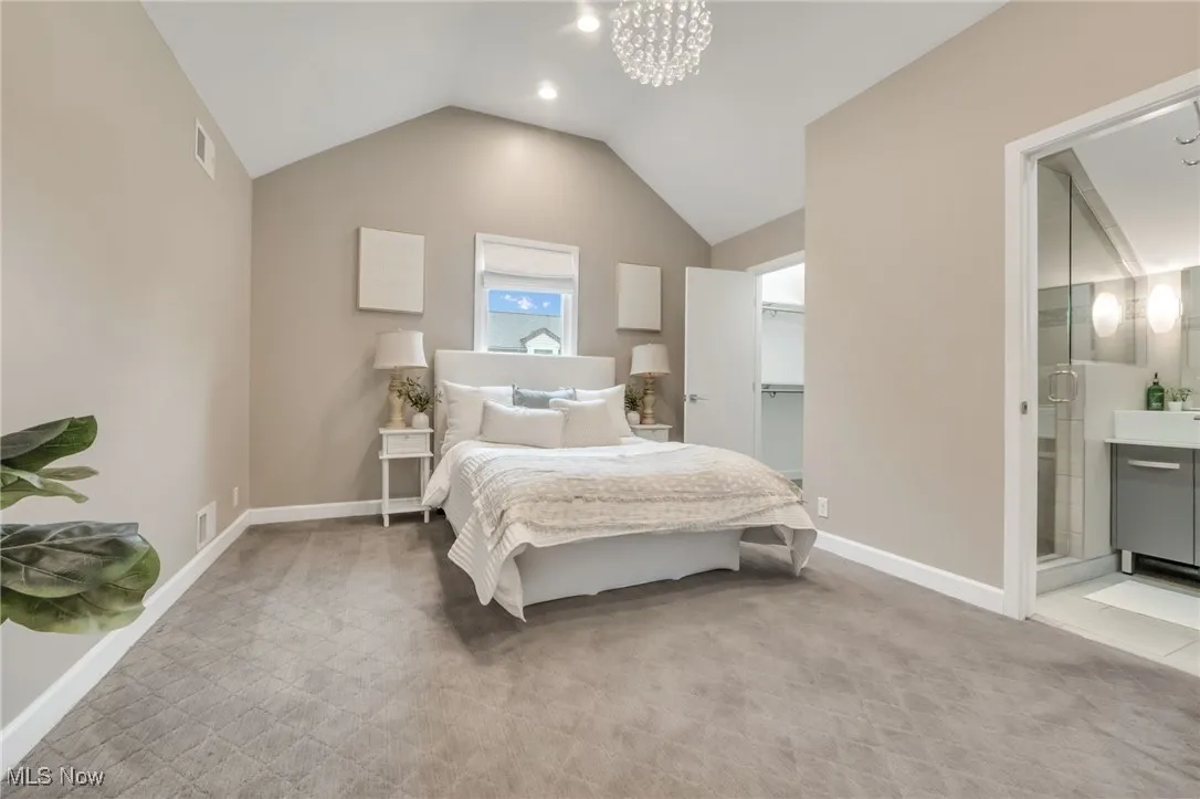 Bedroom with lofted ceiling, baseboards, carpet flooring, ensuite bathroom, and a chandelier