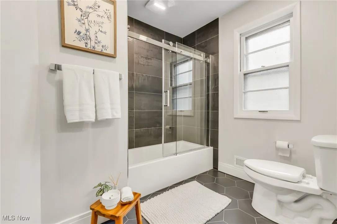 Bathroom with toilet, tile patterned flooring, baseboards, and bath / shower combo with glass door