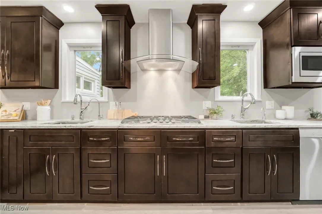 Kitchen with wall chimney range hood, stainless steel appliances, a sink, dark brown cabinetry, and recessed lighting
