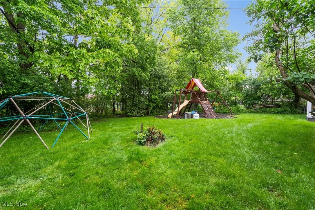 View of green lawn with a playground and view of scattered trees