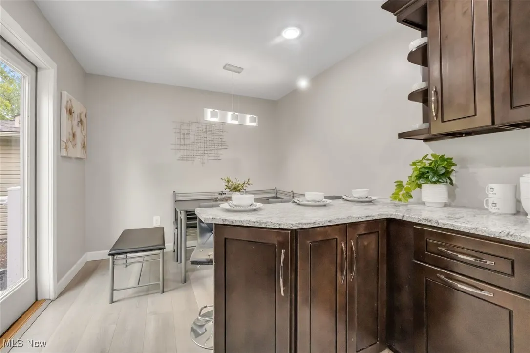 Kitchen featuring dark brown cabinetry, a peninsula, light wood-style flooring, light stone counters, and recessed lighting