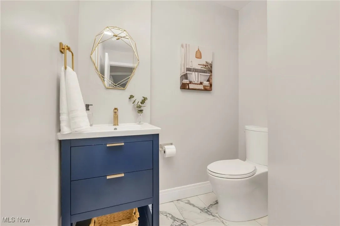Half bathroom with marble look tiles, toilet, vanity, and baseboards