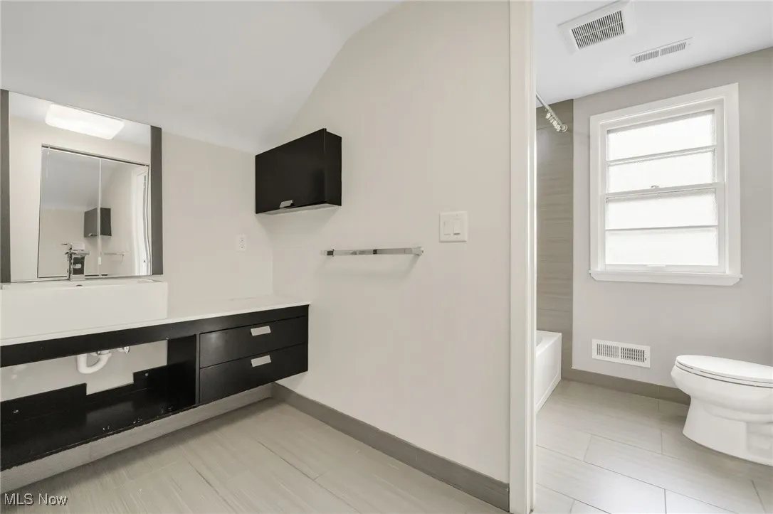 Full bath featuring vanity, baseboards, toilet,  shower combination, and vaulted ceiling