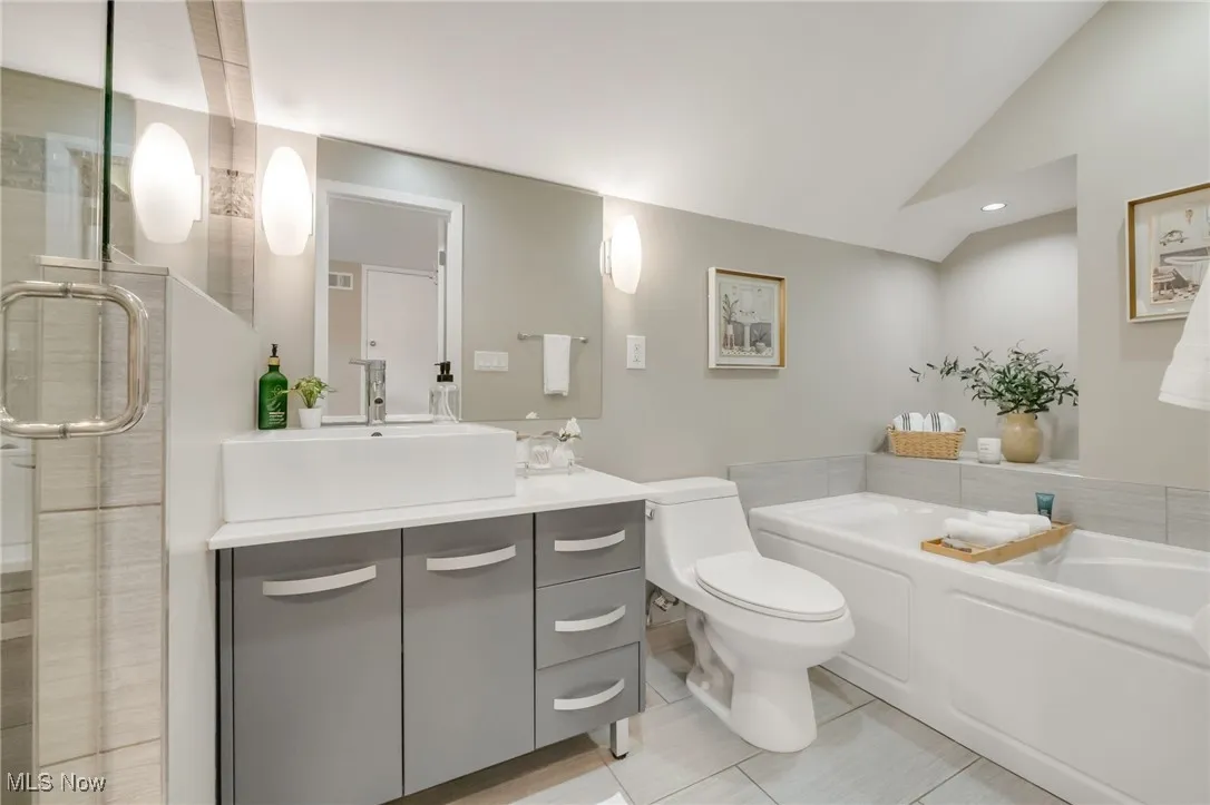 Full bathroom featuring vanity, toilet, a bath, lofted ceiling, and a stall shower