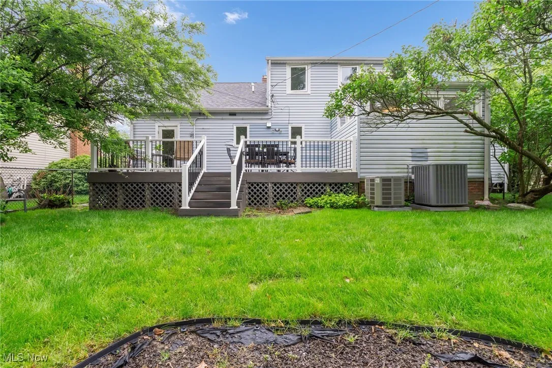 Rear view of property with central AC unit, a wooden deck, and a lawn