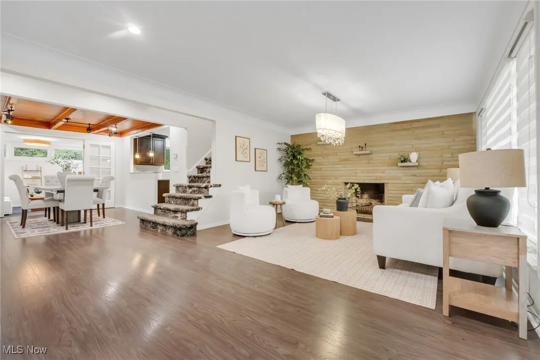 Living room featuring stairs, wood finished floors, a fireplace, wood walls, and beamed ceiling