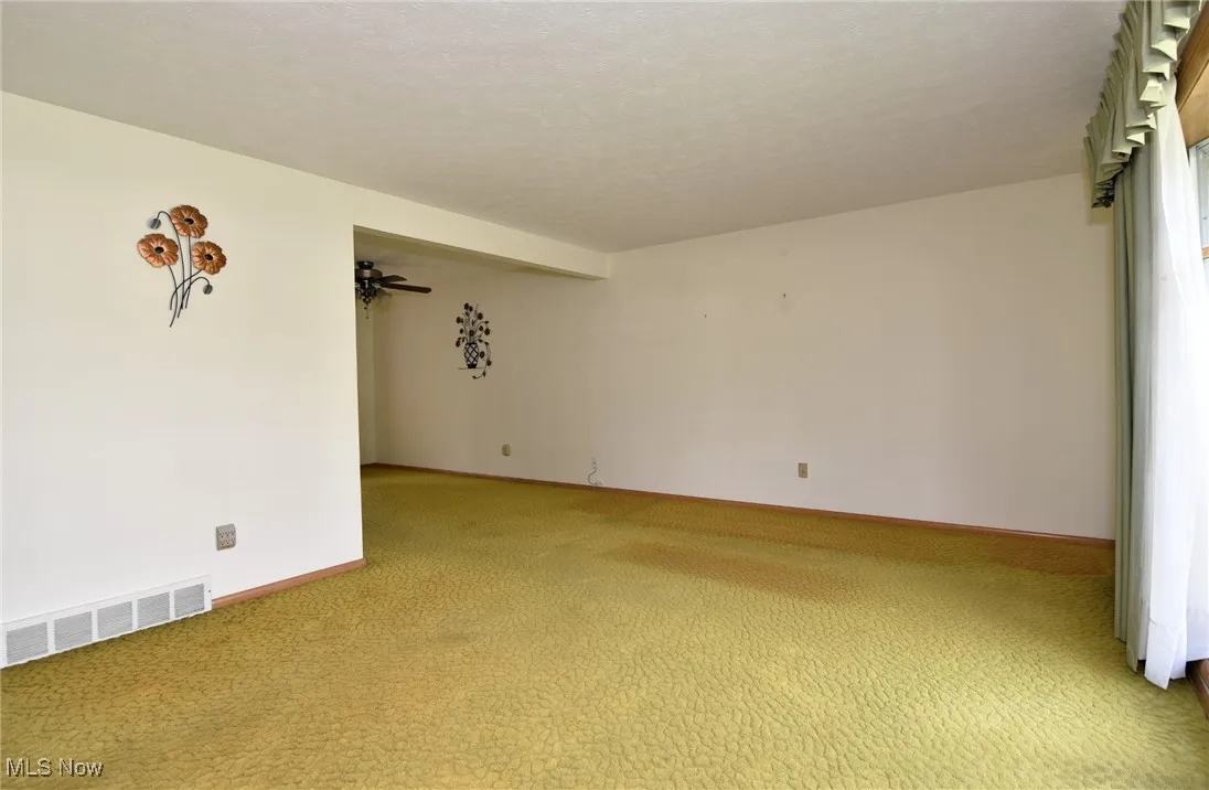 Empty room featuring light colored carpet, baseboards, and ceiling fan