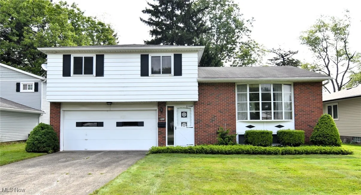 Split level home featuring brick siding, a front yard, an attached garage, and driveway
