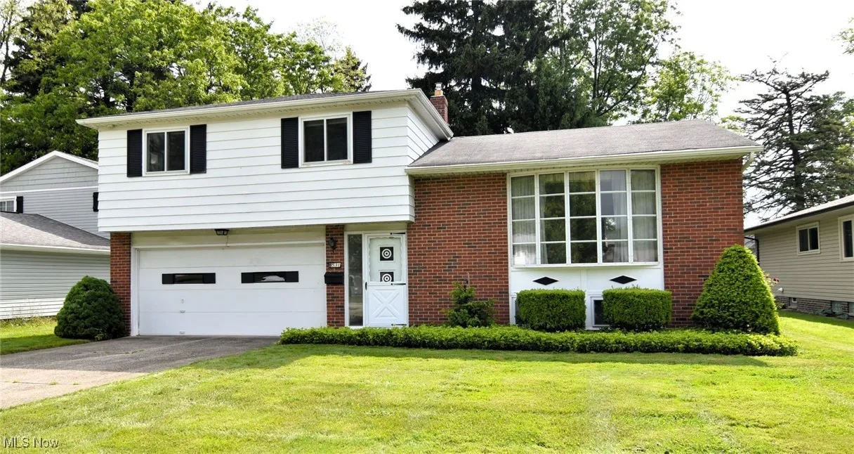 Split level home with brick siding, driveway, a chimney, a front yard, and an attached garage