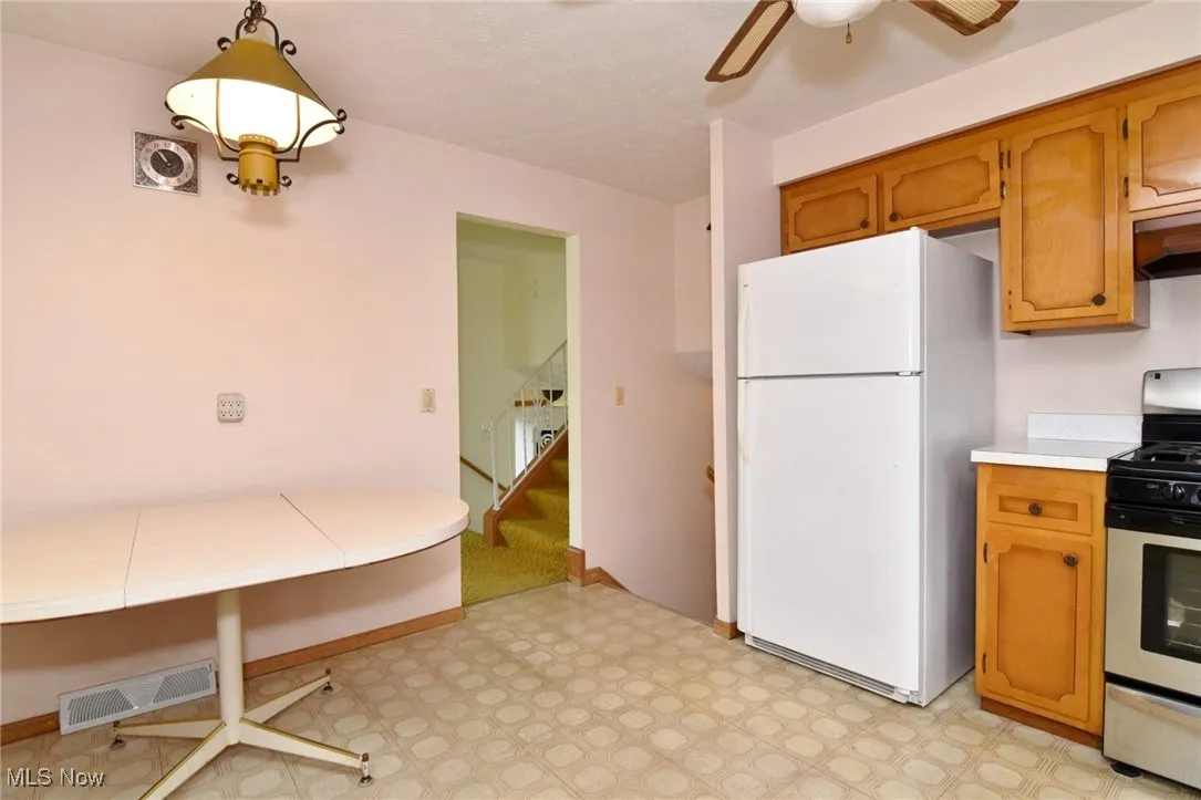 Kitchen with freestanding refrigerator, gas stove, light floors, light countertops, and ceiling fan
