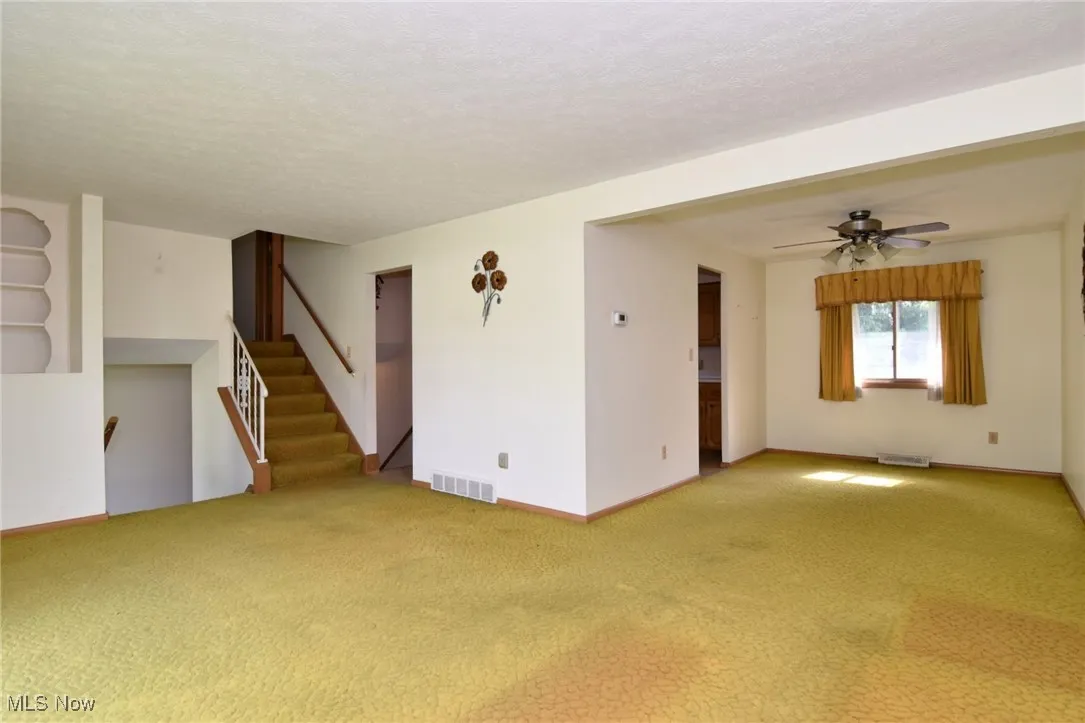 Empty room featuring carpet floors, a ceiling fan, a textured ceiling, stairs, and baseboards