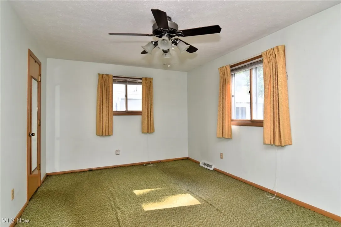 Carpeted empty room with ceiling fan, baseboards, and a textured ceiling